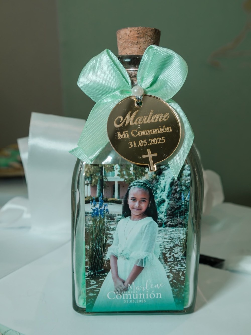 Botellita de recuerdo con lazo verde menta, medalla dorada grabada y foto de la niña de comunión