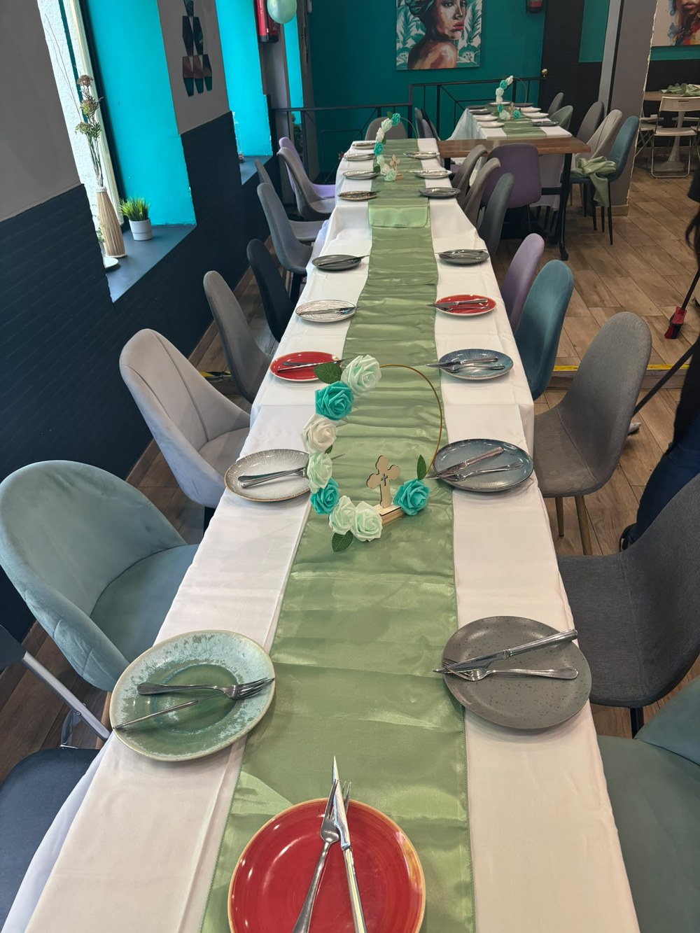 Mesa larga con mantel blanco, camino verde satinado y centros de rosas con cruz
